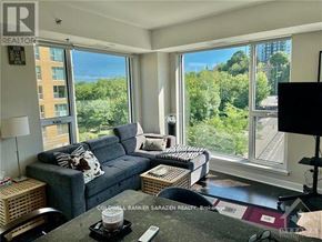 Ottawa condo for rent - A living room with a grey couch and a large window overlooking a forest.