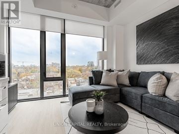 Toronto (Kensington-Chinatown) condo for rent - A modern living room with a grey couch and a large window overlooking a cityscape.