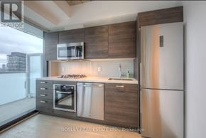 Toronto (Waterfront Communities) condo for rent - A modern kitchen with a stainless steel refrigerator and wooden cabinets.