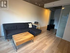 Toronto (Kensington-Chinatown) condo for rent - A living room with a black couch, a wooden coffee table, and a glass door leading to another room.