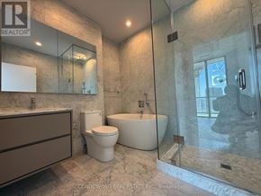 Toronto (Bayview Village) condo for rent - A bathroom with a marble floor and walls, a white bathtub, and a walk-in shower.