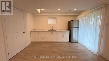 Vaughan (Patterson) apartment for rent - A kitchen with white cabinets and a refrigerator in a room with a white door and a window with blinds.