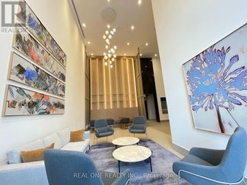 Mississauga (City Centre) condo for rent - A living room with a blue sofa, grey armchairs, and a large abstract painting on the wall.