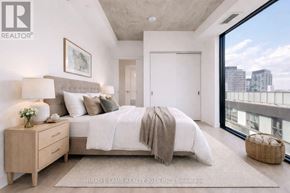 Toronto (Moss Park) condo for rent - A bedroom with a large bed, a nightstand, and a balcony overlooking a cityscape.
