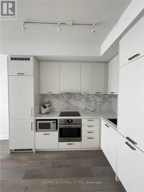 Vaughan (Concord) condo for rent - A white kitchen with a marble backsplash and a refrigerator.