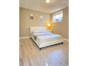 Surrey apartment for rent - A white bed with a grey bedspread is in a room with wooden flooring and a window.