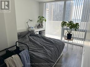 Toronto (Waterfront Communities) condo for rent - A bedroom with a bed, a desk with a lamp, and a potted plant.