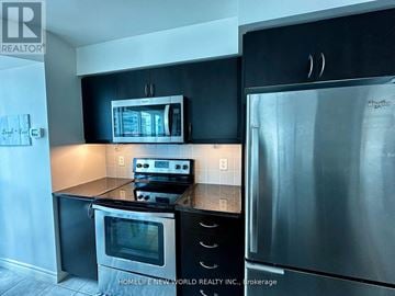 Toronto (Waterfront Communities) condo for rent - A modern kitchen with a stainless steel refrigerator and black cabinets.