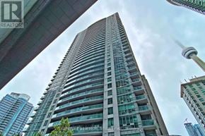 Toronto (Waterfront Communities) condo for rent - A tall building with a glass facade stands in front of a cloudy sky.