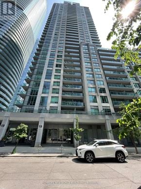 Toronto (Waterfront Communities) condo for rent - A white car is parked in front of a building with a glass facade.