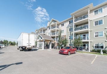 Edmonton apartment for rent - A red car is parked in a parking lot in front of a building.