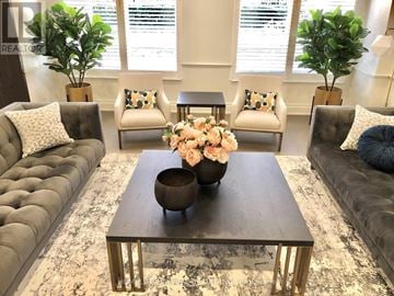 Toronto (Banbury-Don Mills) condo for rent - A living room with a grey couch, a coffee table with a vase of flowers, and two potted plants.