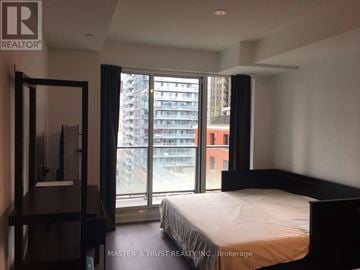 Toronto (Waterfront Communities) condo for rent - A bedroom with a large bed and a view of a city street through the window.