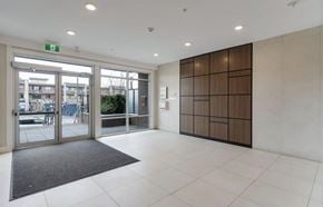 Langley apartment for rent - A hallway with a grey carpet and a glass door leading to a parking lot.