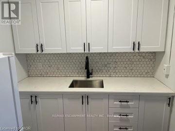 Hamilton (Ainslie Wood) condo for rent - A kitchen with white cabinets and a tiled backsplash.