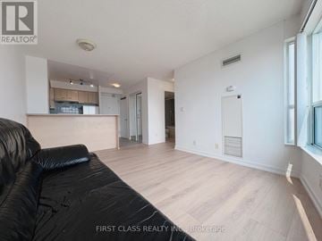Toronto (Woburn) condo for rent - A black leather sofa sits in a spacious living room with hardwood floors and white walls.