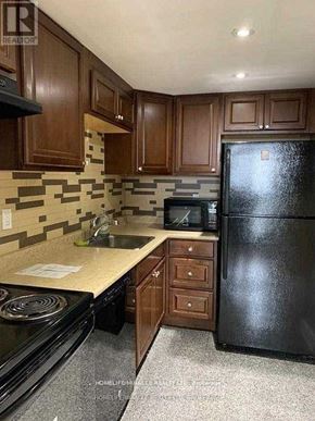 Mississauga (Cooksville) condo for rent - A black refrigerator sits in a kitchen with wooden cabinets and a black stove.