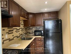Mississauga (Cooksville) condo for rent - A kitchen with brown cabinets and a black fridge.