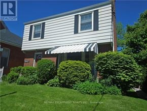 Burlington (Brant) apartment for rent - A house with a white siding and a striped awning is surrounded by green bushes.