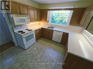 Burlington (Brant) apartment for rent - A kitchen with a white stove top oven and microwave, a white dishwasher, and wooden cabinets.