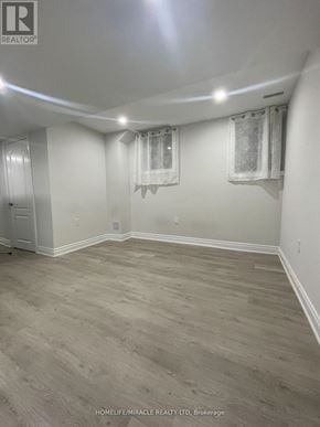 Brampton (Northwest Brampton) apartment for rent - A room with wooden flooring and white walls, with a door on the left and two windows with curtains on the right.