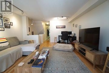 Ottawa townhouse for rent - A living room with a grey sofa, a coffee table with magazines and a remote control on it, a flat screen TV on a wooden stand, and a wooden floor.
