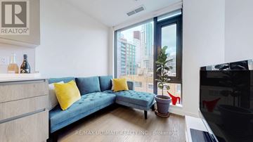 Toronto (Waterfront Communities) condo for rent - A living room with a blue couch and a large window overlooking a cityscape.