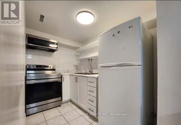 Toronto (Agincourt North) townhouse for rent - A white refrigerator stands in a kitchen with white cabinets and a black stove.
