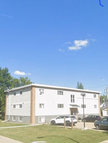 Edmonton apartment for rent - A large white building with a grey roof and a parking lot in front.