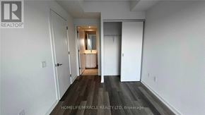 Toronto (Moss Park) condo for rent - A room with white walls and wooden flooring, with a door on the left and a mirror on the right.