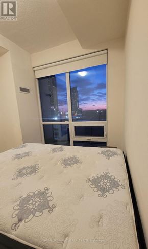 Mississauga (Creditview) condo for rent - A bedroom with a bed, a window with a view of a cityscape at night, and a small table with a lamp.