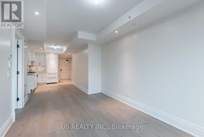 Ottawa condo for rent - A spacious room with wooden flooring and white walls, leading to a kitchen area.