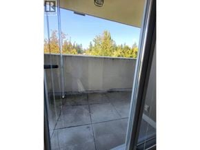 Burnaby apartment for rent - A balcony with a glass door leading to a concrete wall and trees in the background.