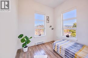 Maple Ridge apartment for rent - A bedroom with a bed, a potted plant, and a window overlooking a cityscape.