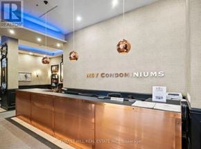 Toronto (Waterfront Communities) condo for rent - The lobby of a building with a copper reception desk and a sign that reads "May Condominiums.".