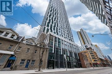 Toronto (Church-Yonge Corridor) condo for rent - A tall building with a glass facade stands in the middle of a city street.