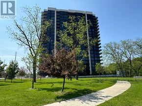 Mississauga (Clarkson) condo for rent - A tall building with a glass facade is surrounded by trees and a grassy area with a walking path.