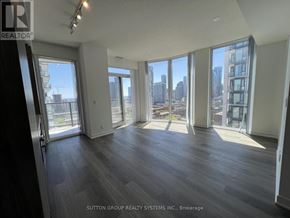 Toronto (Moss Park) condo for rent - A spacious room with wood flooring and large windows overlooking a cityscape.