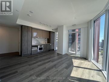 Toronto (Moss Park) condo for rent - A spacious room with wooden flooring and a kitchen area with a sink and stove.