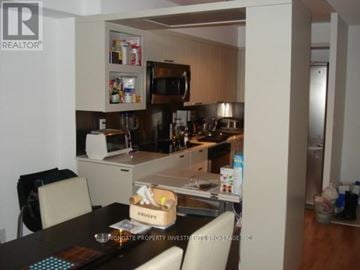 Toronto (Bay Street Corridor) condo for rent - A kitchen with a table and chairs in the foreground and a refrigerator in the background.