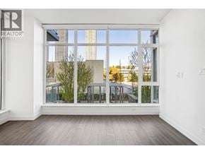 Burnaby apartment for rent - A realtor logo is on the top left corner of a room with a large window.