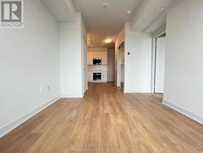 Vaughan (Concord) condo for rent - A spacious room with wooden flooring and white walls, with a kitchen area visible in the distance.