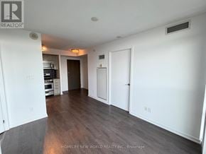 Toronto (Little Portugal) condo for rent - A room with white walls and wooden flooring, with a door on the right and a stove in the background.