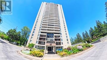 Ottawa condo for rent - A tall apartment building with a parking lot in front and trees in the background.