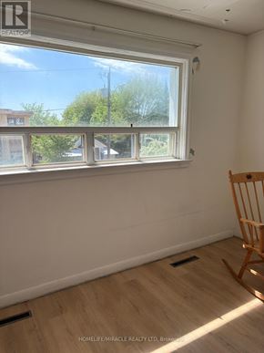 Toronto (Clairlea-Birchmount) apartment for rent - A room with a wooden floor, a window with a view of trees and a building, and a wooden rocking chair.