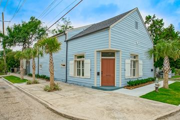 New Orleans apartment for rent - A blue house with a brown door and windows surrounded by greenery.