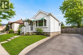 Hamilton apartment for rent - A white house with a green awning is surrounded by a wooden fence and a paved driveway.