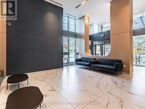 Toronto (Islington-City Centre West) condo for rent - A black sofa with a wooden frame is in the middle of a room with a marble floor.
