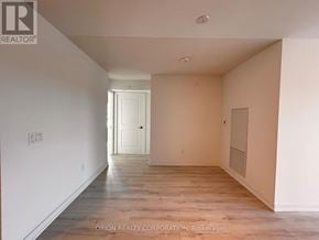 Pickering (Bay Ridges) condo for rent - A spacious room with wooden flooring and white walls, with a doorway leading to another room.