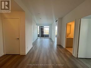 Toronto (South Parkdale) condo for rent - A spacious room with wooden floors and white walls, with a door on the left and a kitchen area on the right.